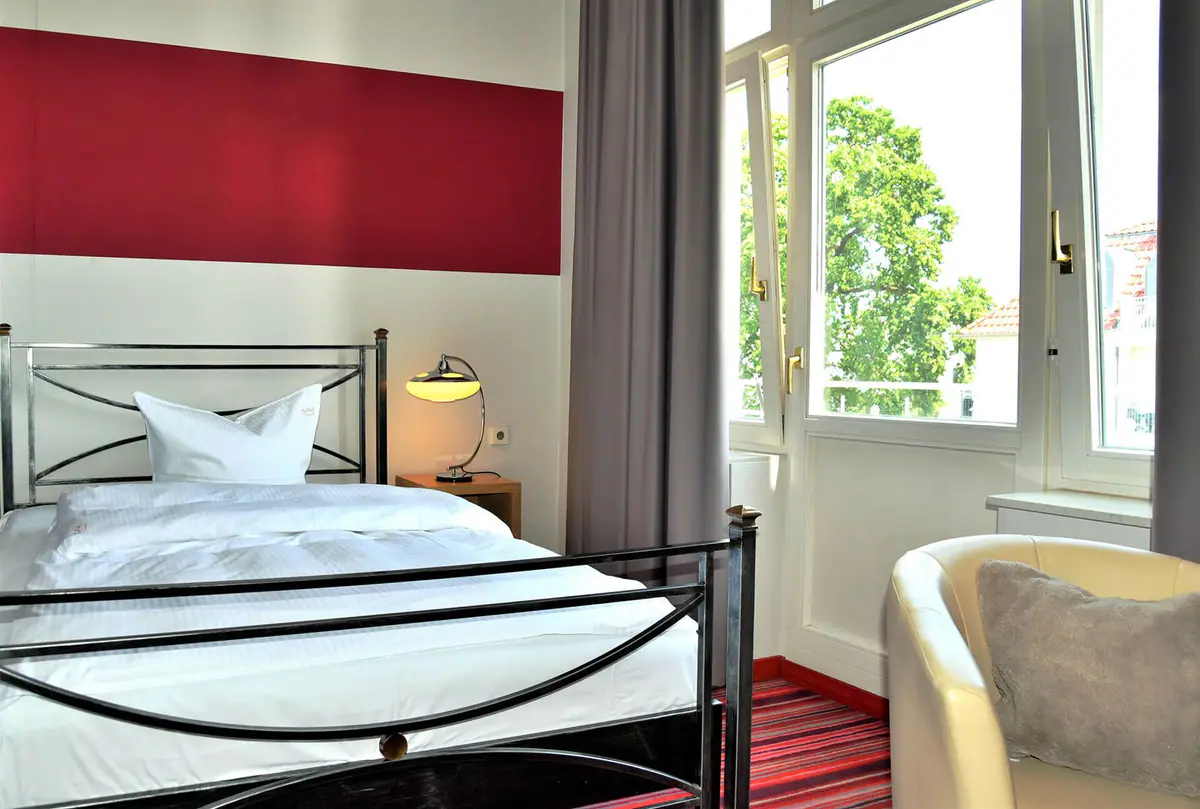 Einzelzimmer mit Metallbett vor roter Wand